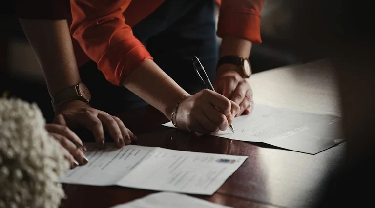 Pessoas assinam contrato de compra e venda de imóvel com advogado imobiliário em mesa de reunião profissional