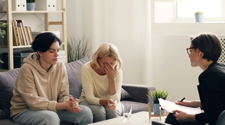 Advogado para Compra de Imóvel de Alto Valor: profissional de óculos segurando documento conversa com duas mulheres sentadas