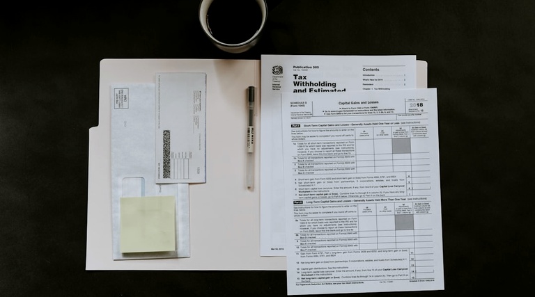 Como travar o patrimônio do devedor: Documentos fiscais e formulários judiciais organizados sobre mesa com caneta e café