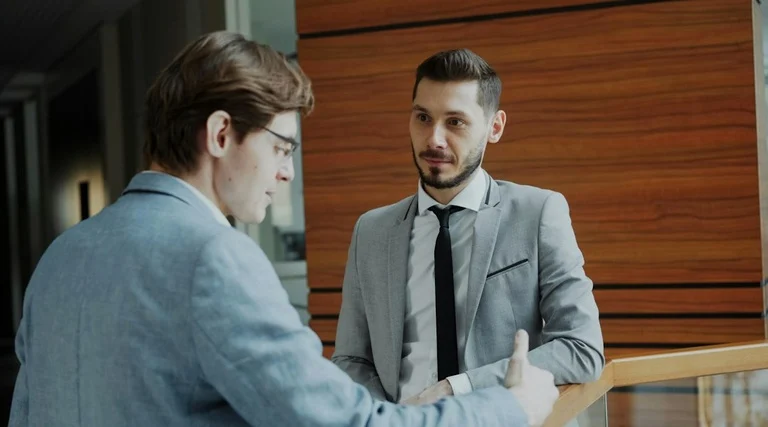 Golpe da falsa central bancária conversa profissional Golpe da falsa central bancária: dois homens de terno conversando em ambiente corporativo com parede de madeira
